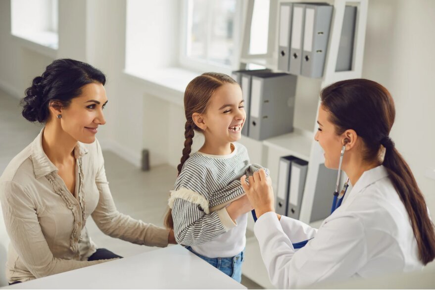 Una madre y su hija en una consulta médica, junto a una profesional de la salud