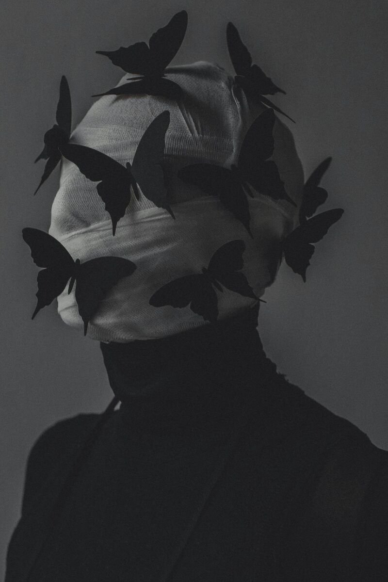 Retrato en blanco y negro de una persona con el rostro cubierto por mariposas negras